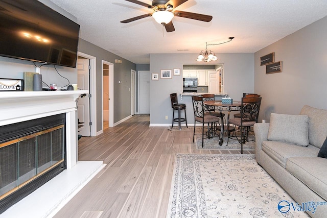 4967 Seven Pine Cir Unit 4967, Huntsville, AL 35816 - living room featuring a ceiling fan, light wood-style flooring, a glass covered fireplace, a chandelier, and baseboards
