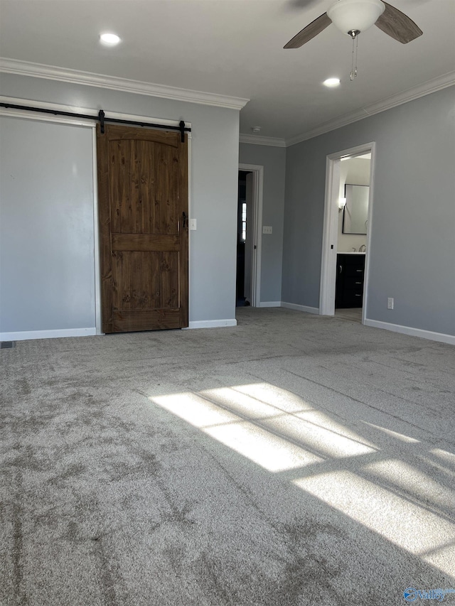 interior space with a barn door, ornamental molding, carpet, and ceiling fan