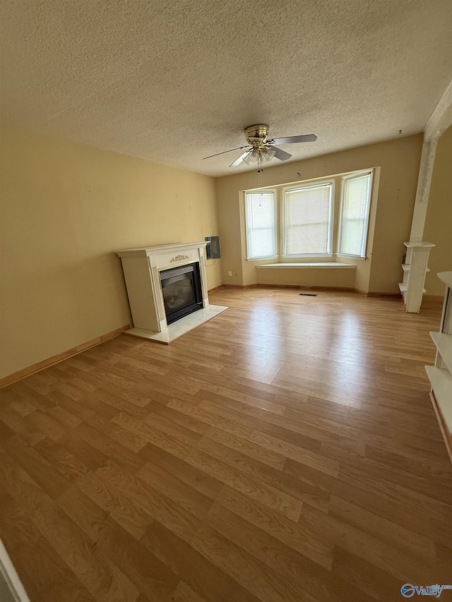 186 Brady Dr, Hazel Green, AL 35750 - unfurnished living room with a textured ceiling, light wood-style flooring, a glass covered fireplace, a ceiling fan, and baseboards