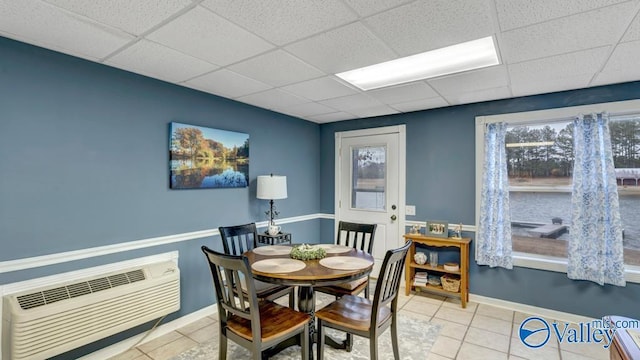 dining space with light tile patterned flooring, an AC wall unit, and a drop ceiling