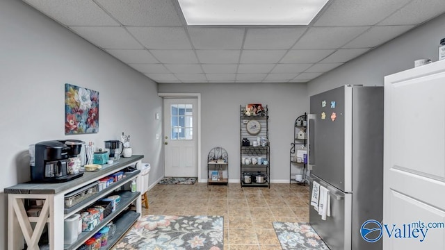 interior space featuring stainless steel refrigerator, a paneled ceiling, and light tile patterned flooring