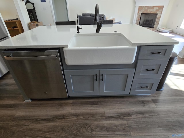 kitchen featuring gray cabinetry, sink, dark wood-type flooring, stainless steel dishwasher, and an island with sink