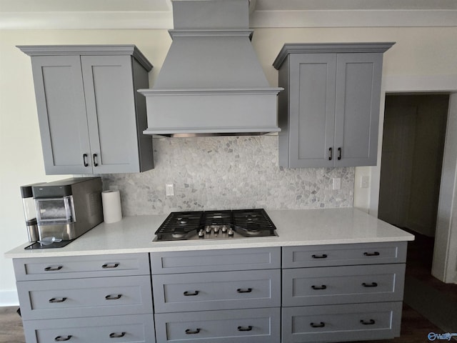 kitchen with backsplash, gray cabinets, stainless steel gas stovetop, and custom exhaust hood