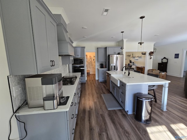 kitchen featuring sink, stainless steel appliances, dark wood-type flooring, pendant lighting, and a center island with sink