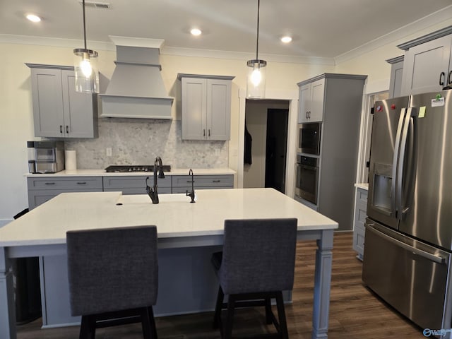 kitchen with pendant lighting, custom range hood, a kitchen island with sink, and appliances with stainless steel finishes