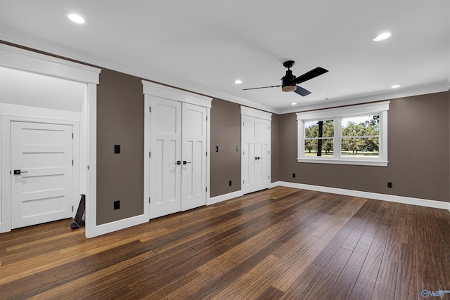 unfurnished bedroom with ornamental molding, dark wood-type flooring, two closets, and ceiling fan