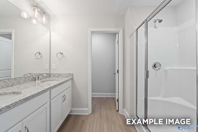 full bath featuring a stall shower, a sink, wood finished floors, and baseboards