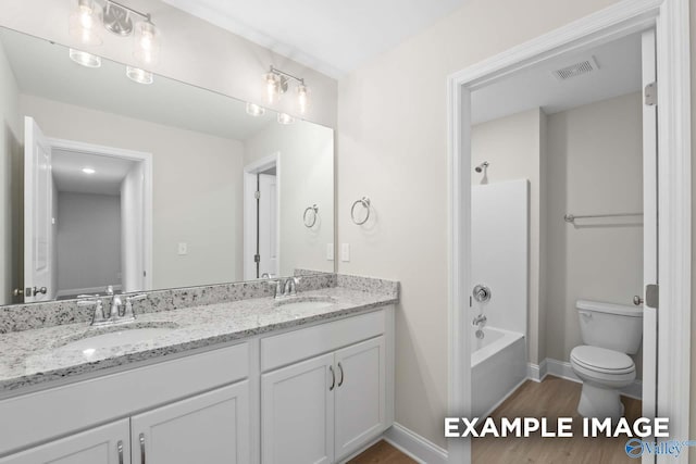 full bathroom with wood finished floors, double vanity, toilet, a sink, and visible vents