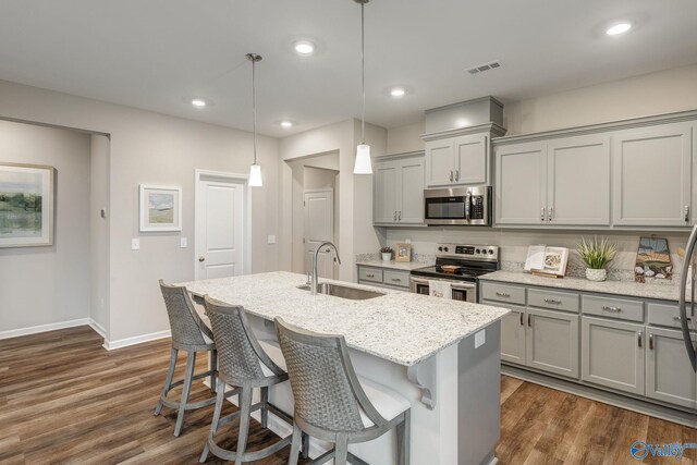 kitchen featuring appliances with stainless steel finishes, dark wood-type flooring, sink, decorative light fixtures, and a center island with sink