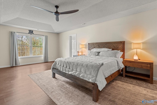 bedroom with a textured ceiling, wood-type flooring, a tray ceiling, and ceiling fan