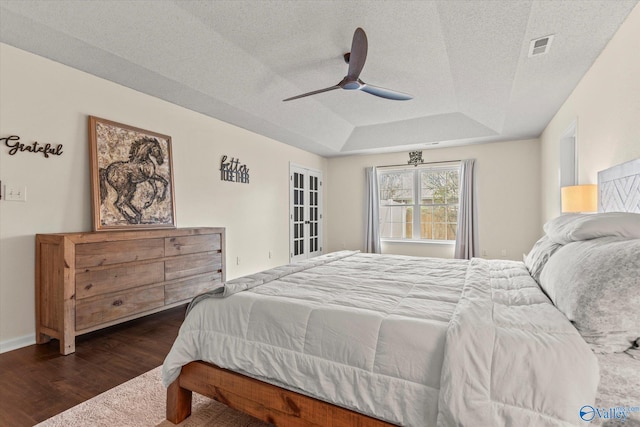 bedroom featuring a textured ceiling, a tray ceiling, dark wood-type flooring, and ceiling fan