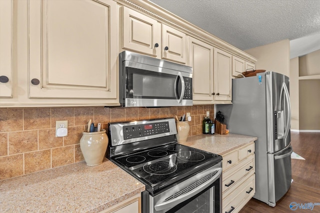 kitchen featuring decorative backsplash, cream cabinets, dark hardwood / wood-style flooring, appliances with stainless steel finishes, and light stone counters