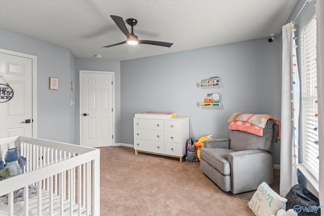 bedroom with a textured ceiling, a nursery area, light colored carpet, and ceiling fan