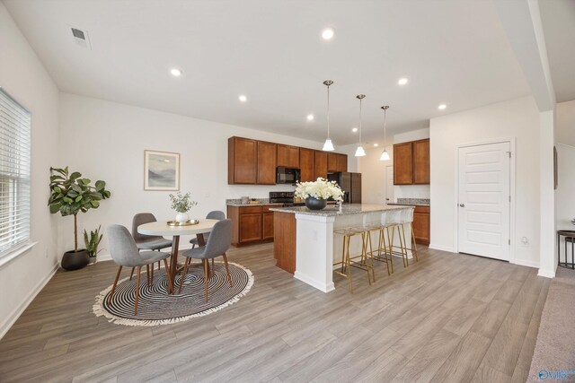 kitchen featuring a breakfast bar area, black appliances, light hardwood / wood-style flooring, a kitchen island with sink, and hanging light fixtures