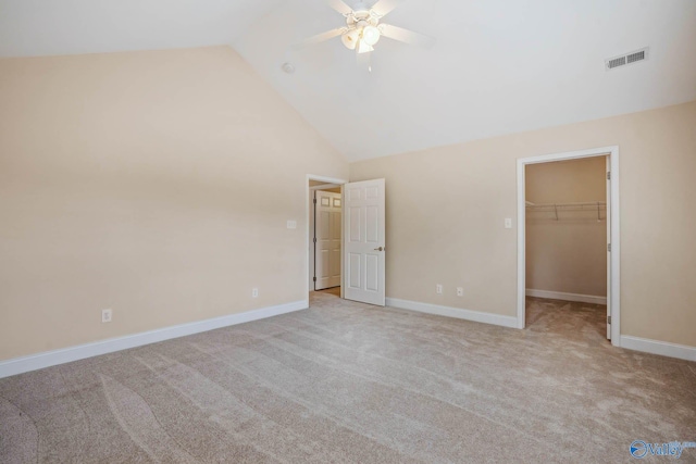 unfurnished bedroom with high vaulted ceiling, a walk in closet, ceiling fan, light carpet, and a closet