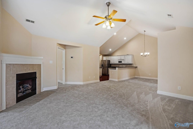 unfurnished living room with light colored carpet, high vaulted ceiling, a tiled fireplace, and ceiling fan with notable chandelier