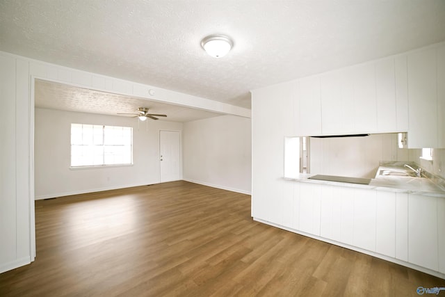 unfurnished living room featuring a ceiling fan, wood finished floors, baseboards, a sink, and a textured ceiling