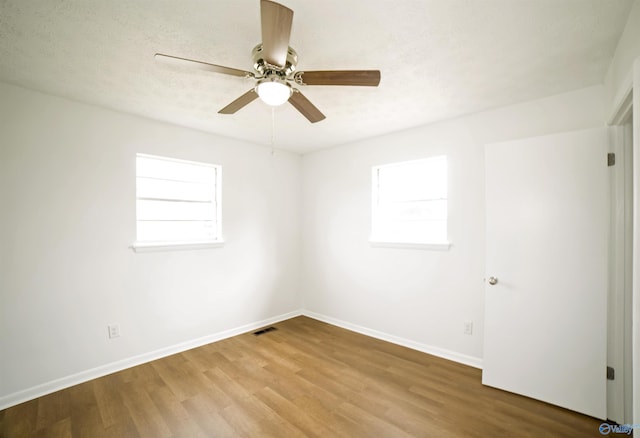 spare room featuring visible vents, plenty of natural light, baseboards, and wood finished floors