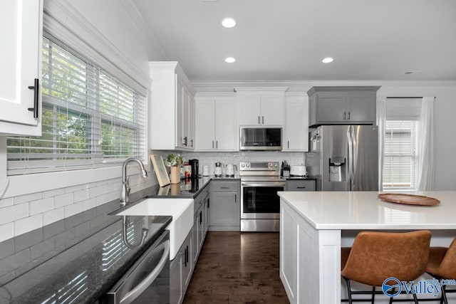 kitchen with a breakfast bar area, crown molding, gray cabinets, stainless steel appliances, and decorative backsplash