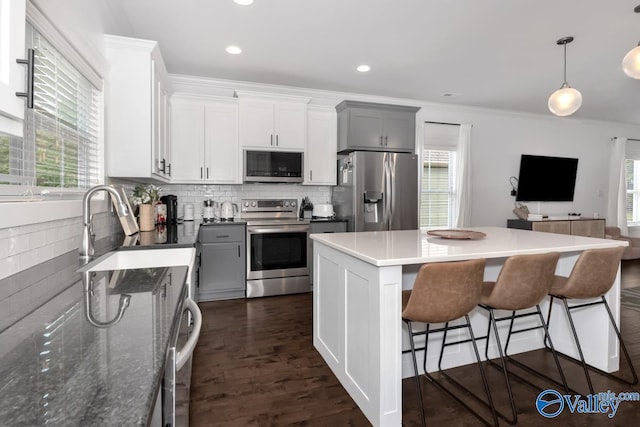 kitchen with sink, white cabinetry, stainless steel appliances, a center island, and decorative light fixtures