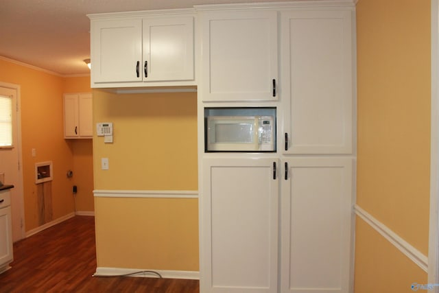 kitchen with dark wood-style flooring, crown molding, white microwave, white cabinetry, and baseboards