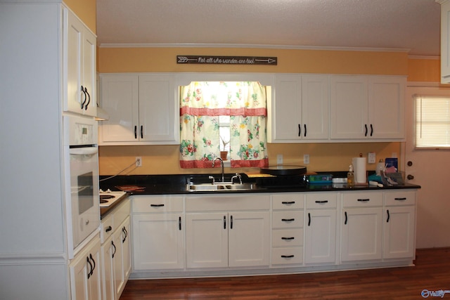 kitchen with ornamental molding, dark countertops, a sink, and white cabinetry