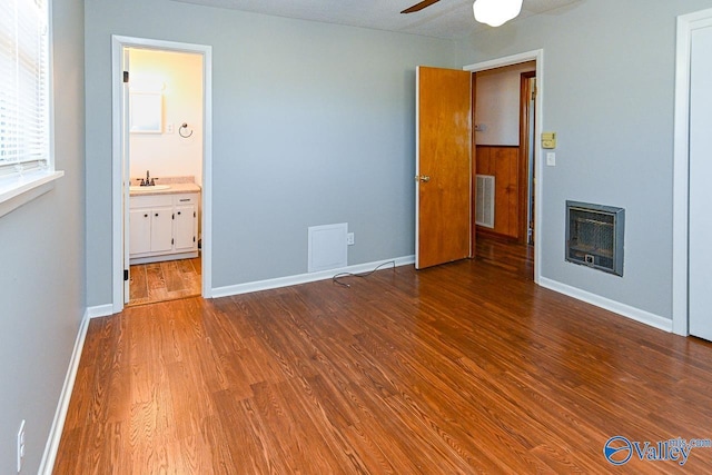 unfurnished bedroom with a fireplace, heating unit, a sink, wood finished floors, and baseboards