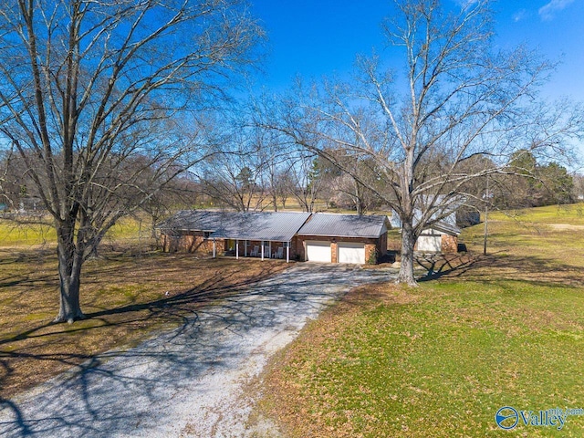 view of front of property featuring an attached garage, metal roof, a front lawn, and gravel driveway