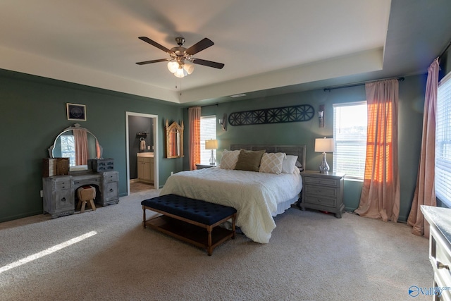 bedroom featuring a raised ceiling, light carpet, a ceiling fan, and connected bathroom