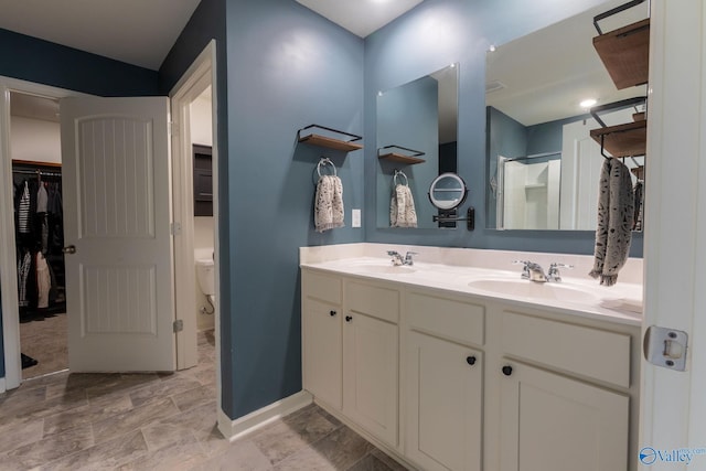 bathroom with a walk in closet, double vanity, a sink, and toilet