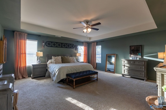 bedroom with a tray ceiling, carpet flooring, ceiling fan, and multiple windows