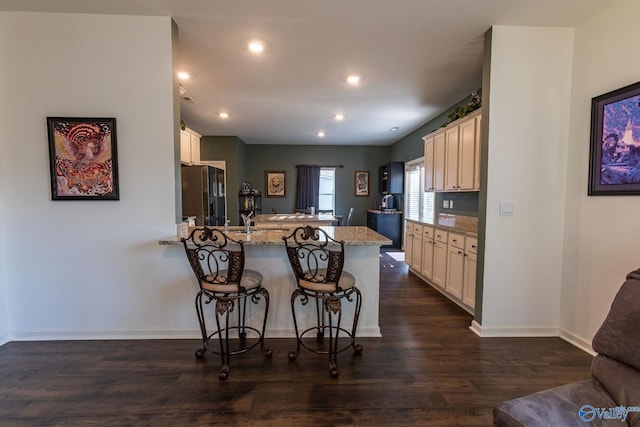 kitchen with a breakfast bar, light stone counters, a peninsula, black refrigerator with ice dispenser, and dark wood-type flooring