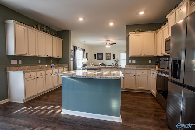 kitchen with ceiling fan, a peninsula, dark wood-style floors, stainless steel appliances, and light stone counters