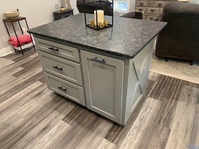 kitchen with gray cabinetry, dark hardwood / wood-style floors, a kitchen island, and dark stone countertops