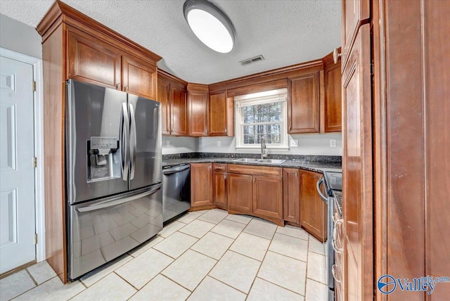 kitchen featuring a textured ceiling, stainless steel appliances, sink, light tile patterned floors, and dark stone countertops