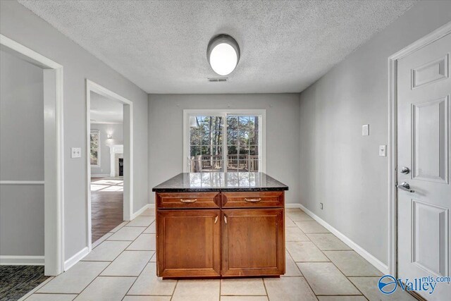 kitchen with a center island, light tile patterned floors, a textured ceiling, and dark stone counters