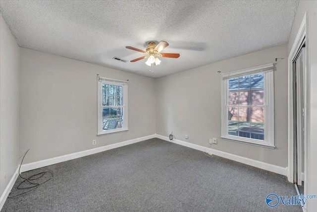 empty room featuring ceiling fan, dark carpet, and a textured ceiling