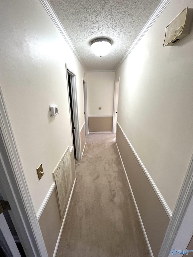 hallway with crown molding, light colored carpet, visible vents, a textured ceiling, and baseboards