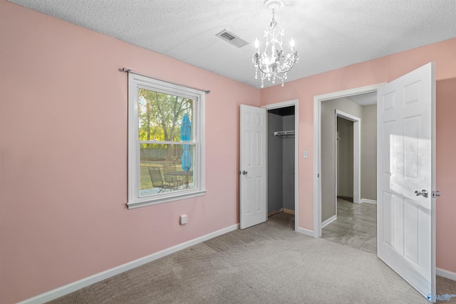 unfurnished bedroom featuring a textured ceiling, light carpet, an inviting chandelier, and a closet