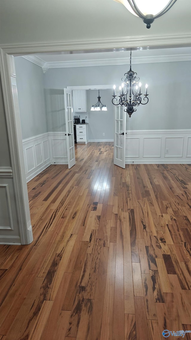 unfurnished dining area with crown molding, wood-type flooring, a chandelier, and french doors