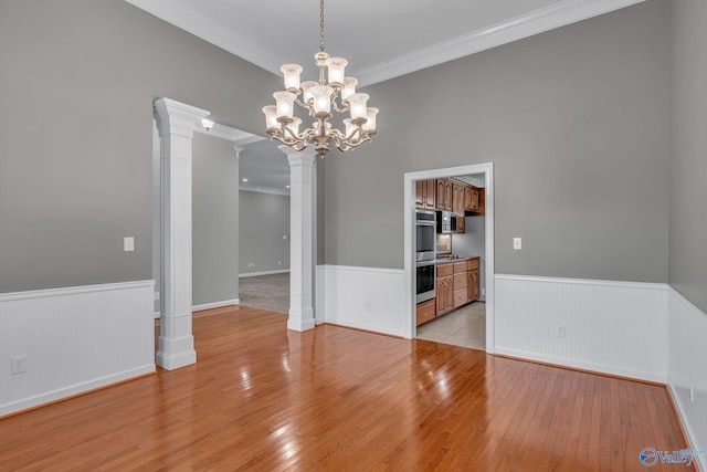 unfurnished dining area with light hardwood / wood-style floors, an inviting chandelier, ornamental molding, and decorative columns