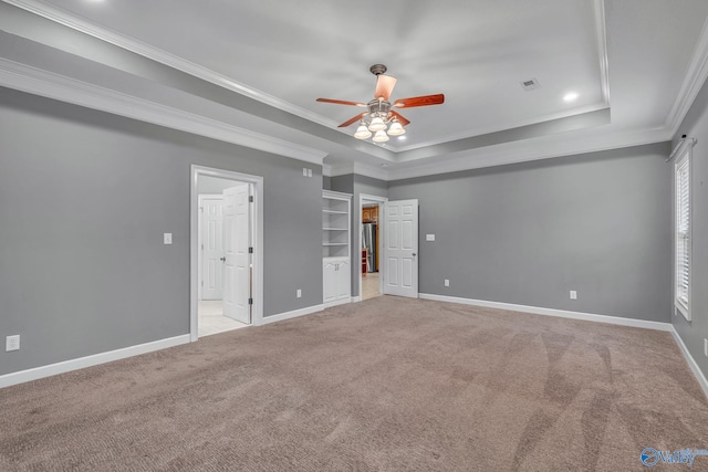 unfurnished bedroom with ornamental molding, a tray ceiling, light colored carpet, ceiling fan, and a spacious closet