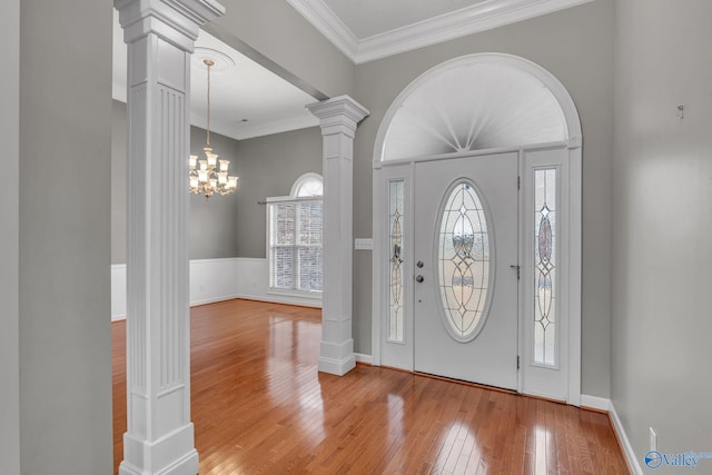 foyer entrance featuring decorative columns, light hardwood / wood-style flooring, ornamental molding, and a notable chandelier