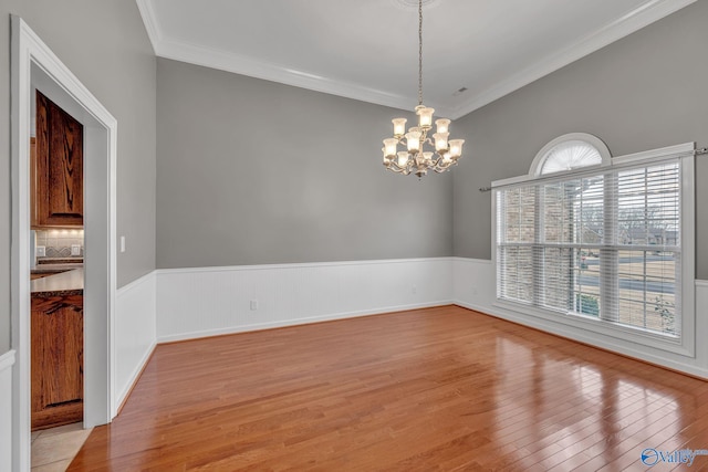 unfurnished dining area featuring a wealth of natural light, crown molding, light hardwood / wood-style floors, and an inviting chandelier