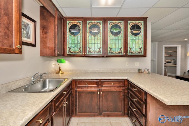 kitchen featuring kitchen peninsula, a paneled ceiling, light tile patterned flooring, and sink