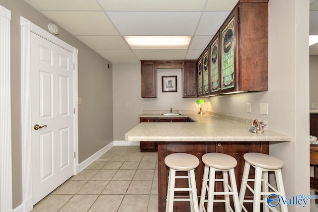 kitchen with light tile patterned flooring, sink, kitchen peninsula, a drop ceiling, and a kitchen breakfast bar