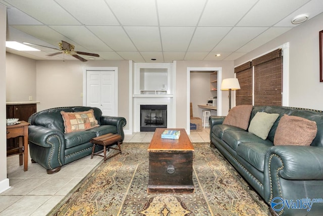 living room featuring ceiling fan, light tile patterned flooring, a drop ceiling, and built in features