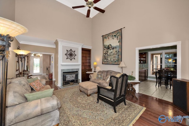 living room featuring a towering ceiling, a fireplace, wood-type flooring, ceiling fan, and ornamental molding