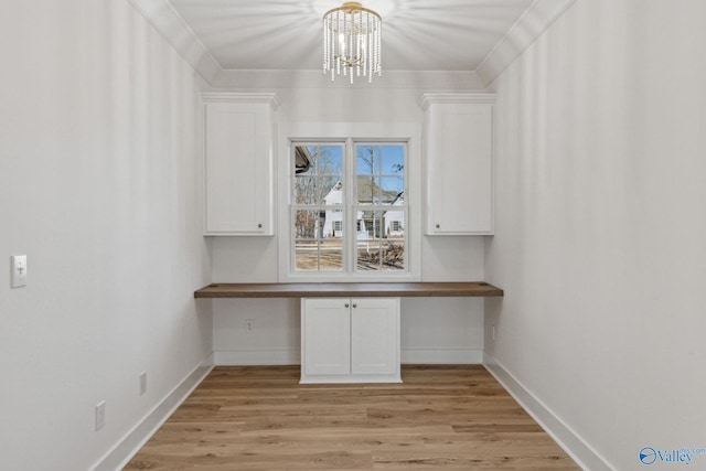 unfurnished office featuring crown molding, built in desk, and light hardwood / wood-style flooring