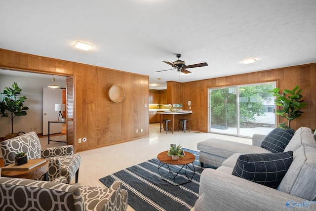 living area with ceiling fan and wood walls